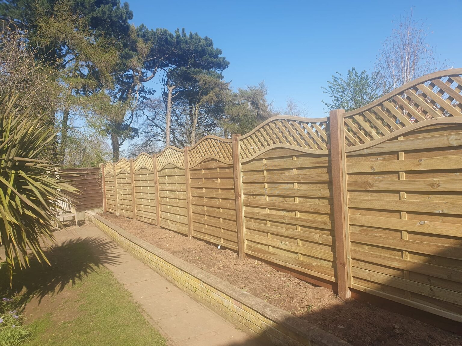 Decorative timber garden fencing with curved trellis panels along a boundary