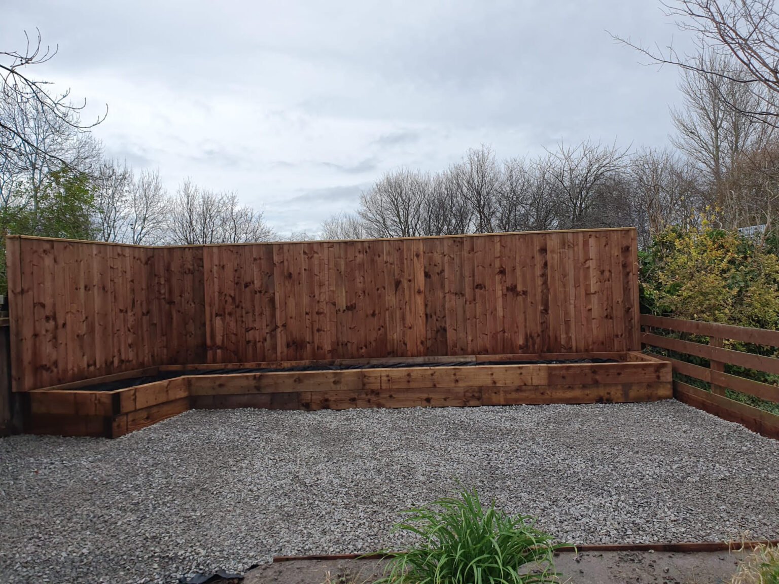 Timber garden fence behind raised wooden beds and a gravel seating area