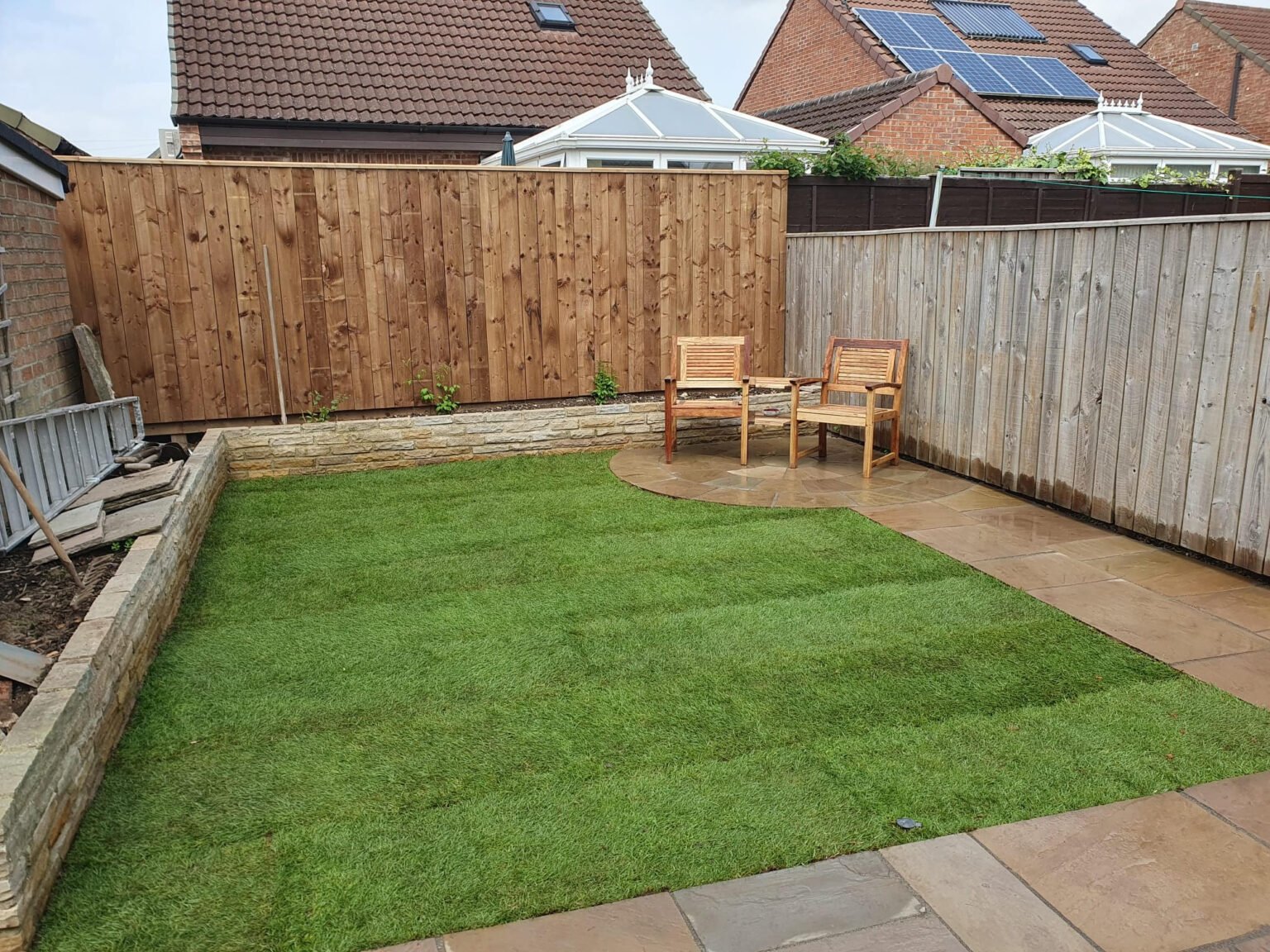 Timber fencing enclosing a garden with a lawn and curved paved seating area